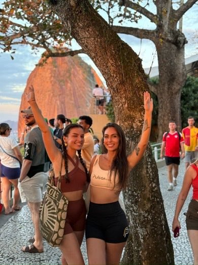 Duas amigas sorrindo durante um rolê ao ar livre, com o Pão de Açúcar ao fundo.